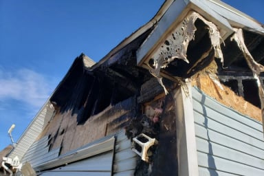 Severely burned residential building corner with exterior damage.