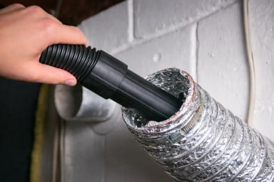 A person using a vacuum hose on metal ducting.
